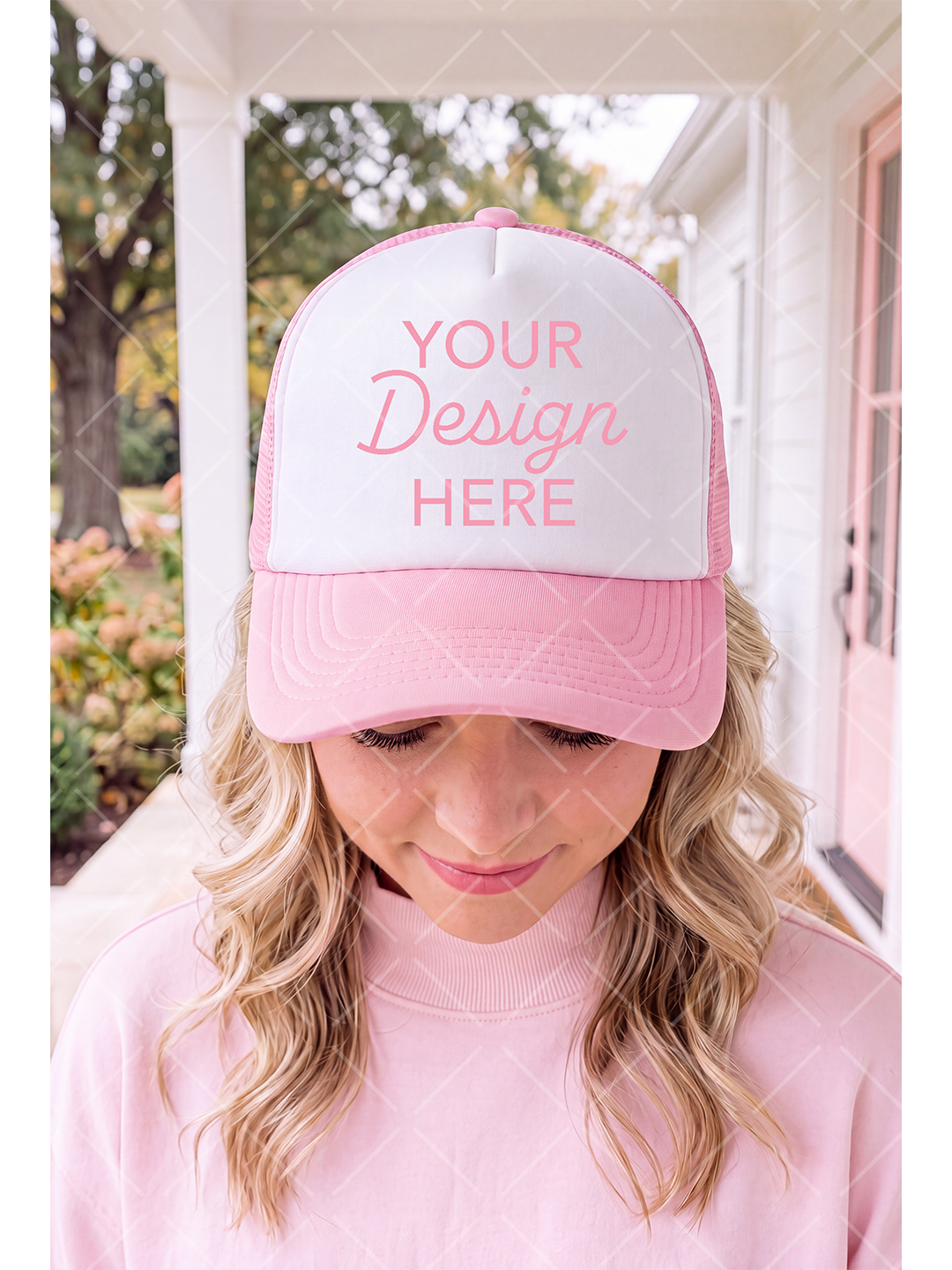 Female model wearing a pink-and-white trucker hat and pink sweatshirt on a softly blurred porch
