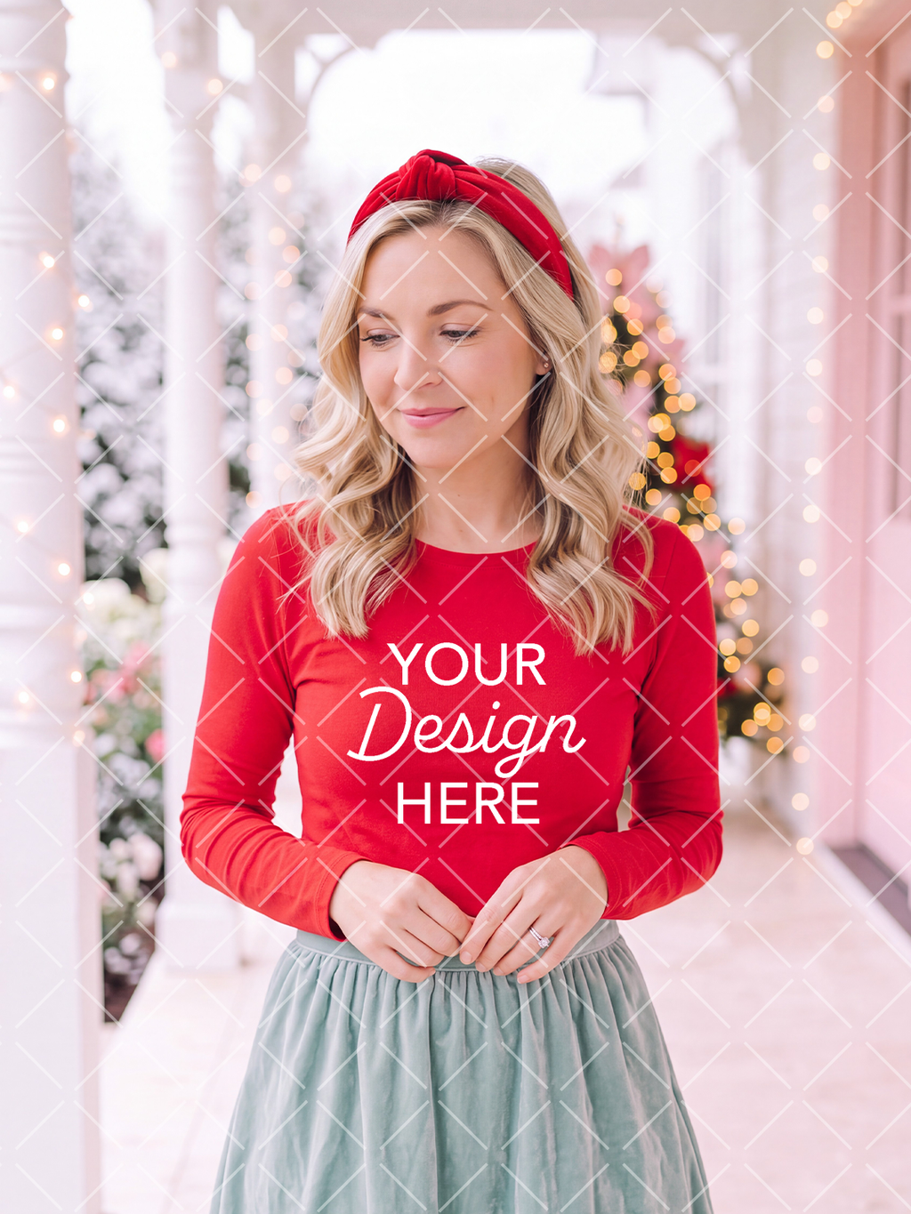 Blonde woman wearing a red long-sleeve shirt and knotted headband in a softly lit pink Christmas setting with decorated trees.